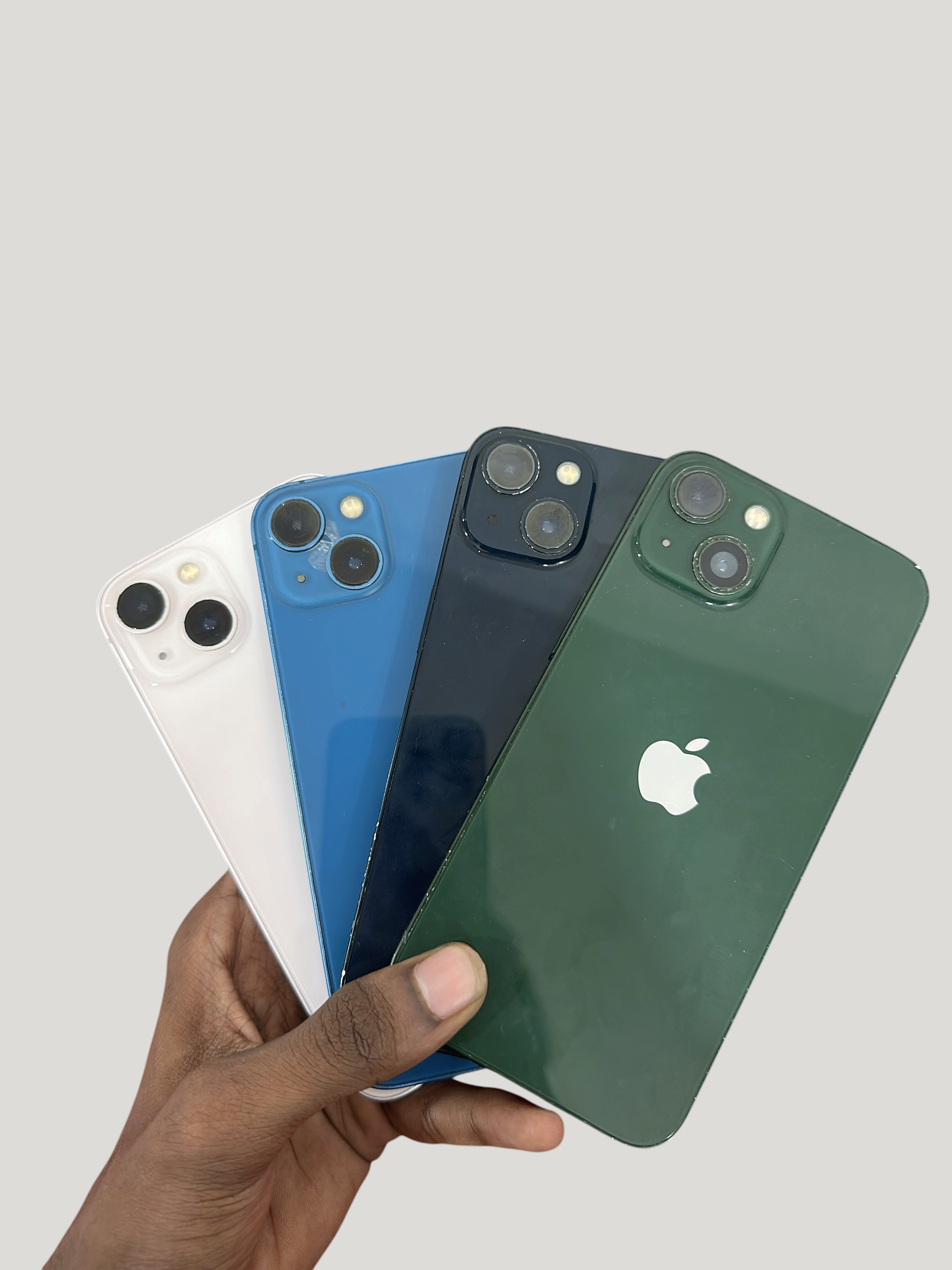 Iphoneio Official Apple iPhone 13 smartphones in white, blue, black, and green held in a hand against black background