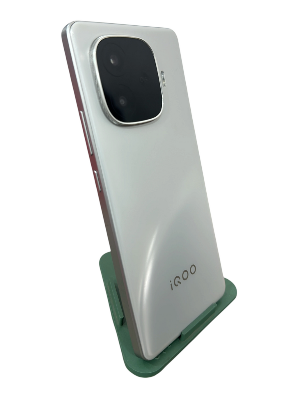 Iphoneio Official iQOO smartphone in pearlescent white with a prominent rear camera module on a green stand.
