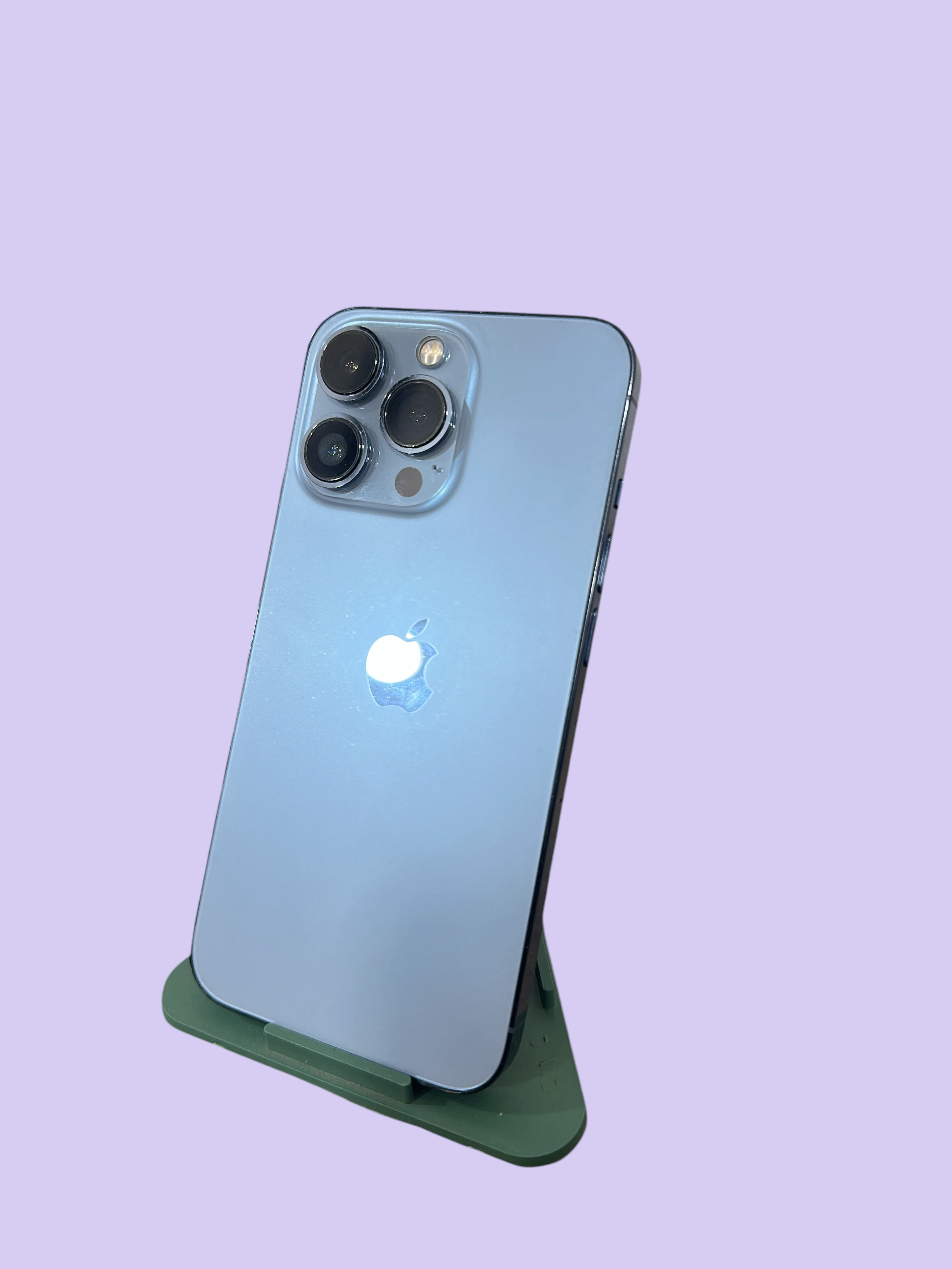 Iphoneio Official light blue smartphone with a triple-camera system on a green stand against a black background
