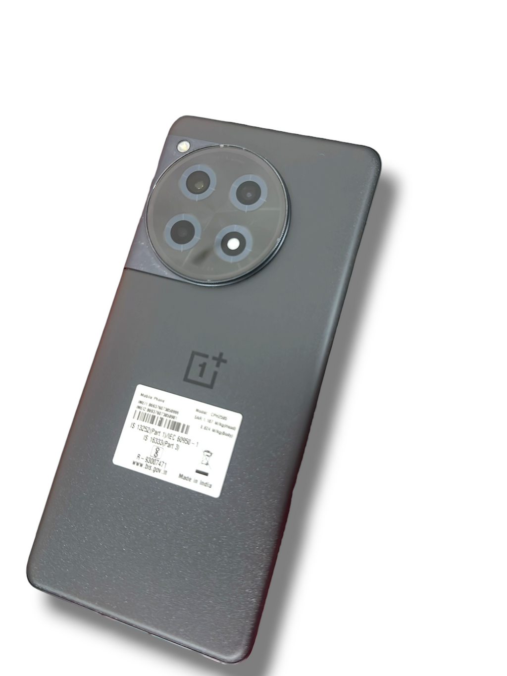 Iphoneio Official OnePlus 12R smartphone in matte black with a circular camera module resting on a red product box.