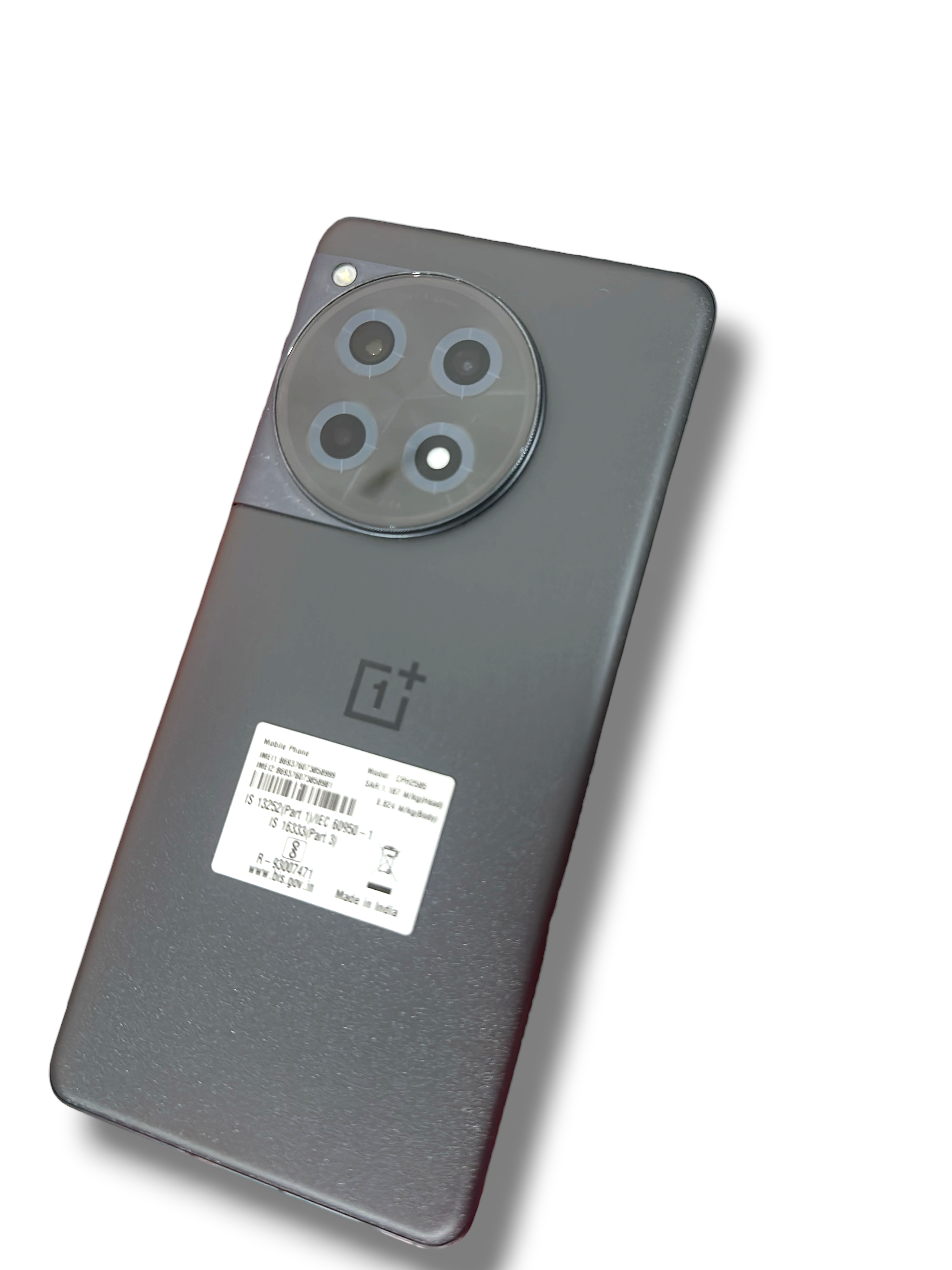 Iphoneio Official OnePlus 12R smartphone in matte black with a circular camera module resting on a red product box.