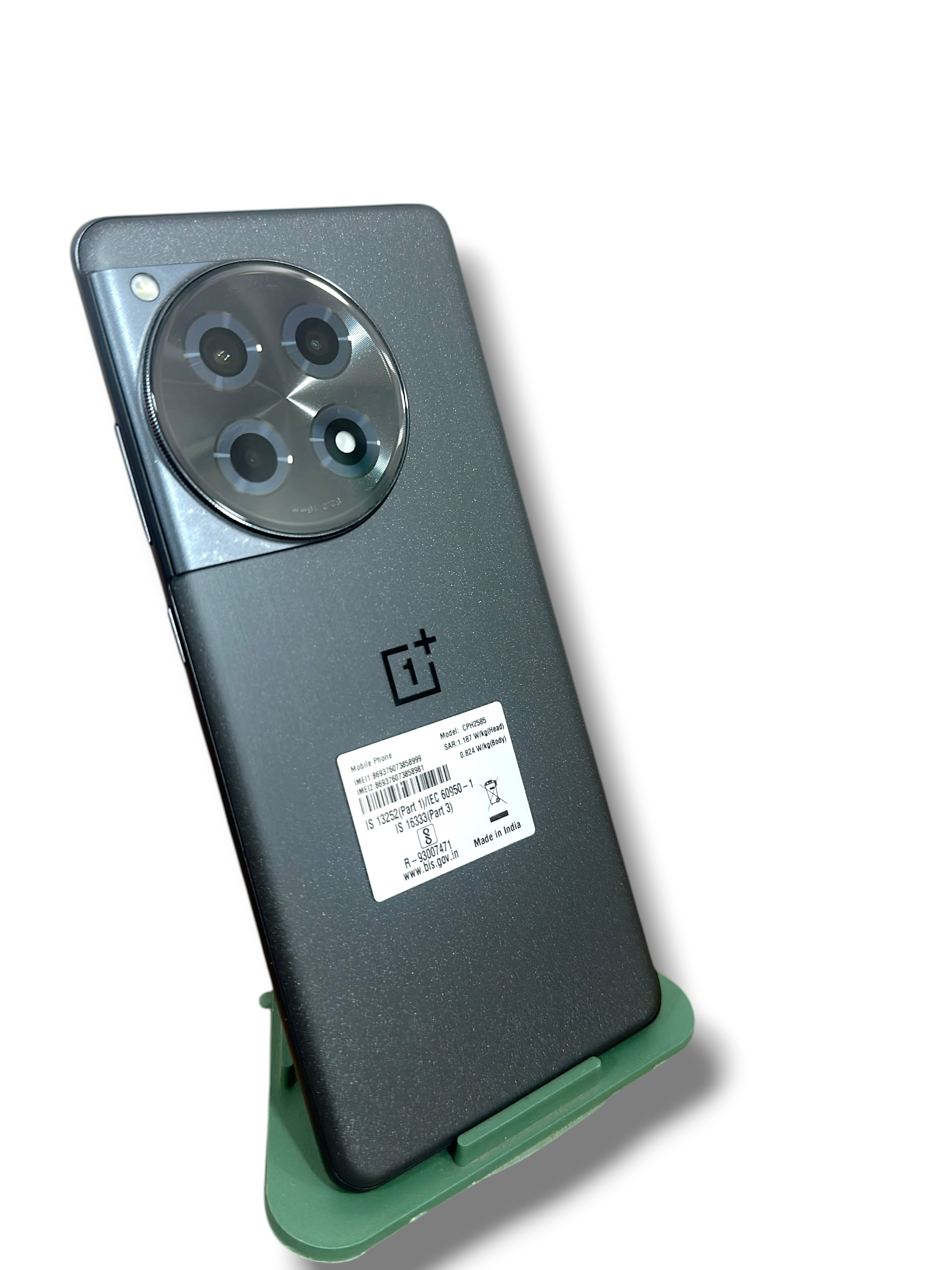 Iphoneio Official OnePlus 12R smartphone in matte grey with a circular triple camera module on a green stand
