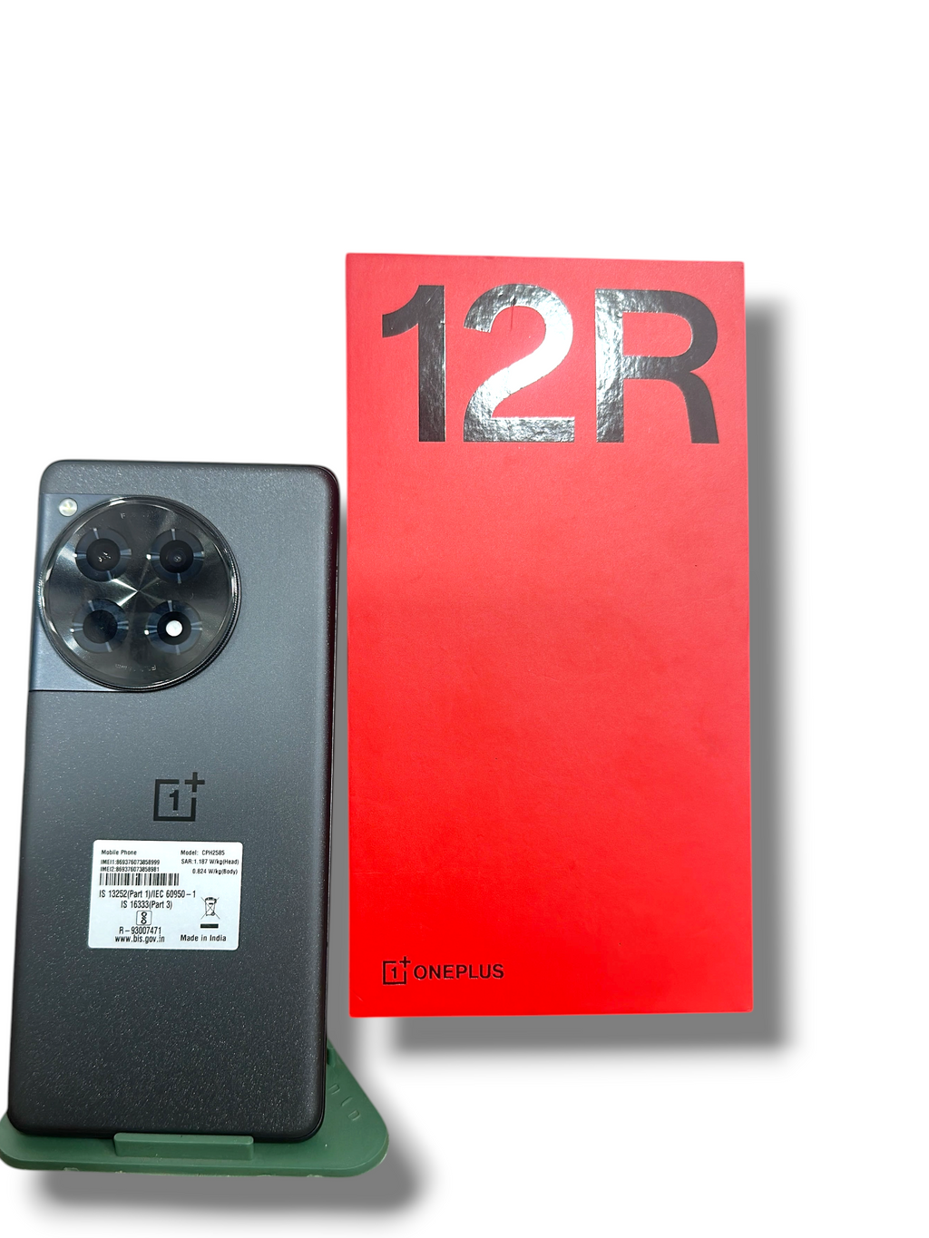 Iphoneio Official OnePlus 12R smartphone in grey with a large circular camera module next to its red retail box.