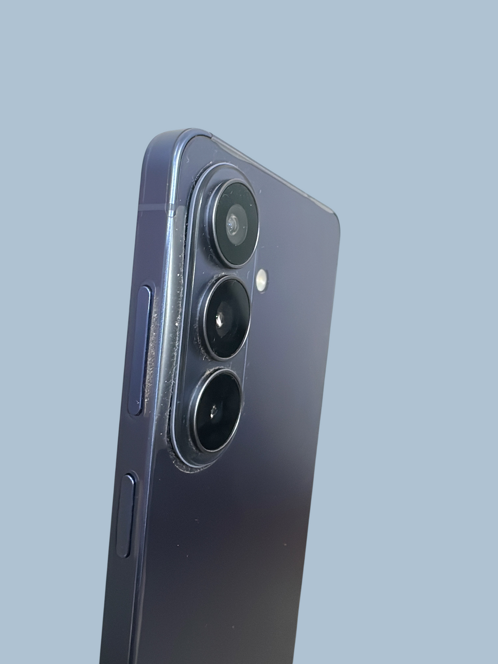 Iphoneio Official Samsung Galaxy S26 smartphone in dark blue with a triple-lens camera system and sleek metal frame.