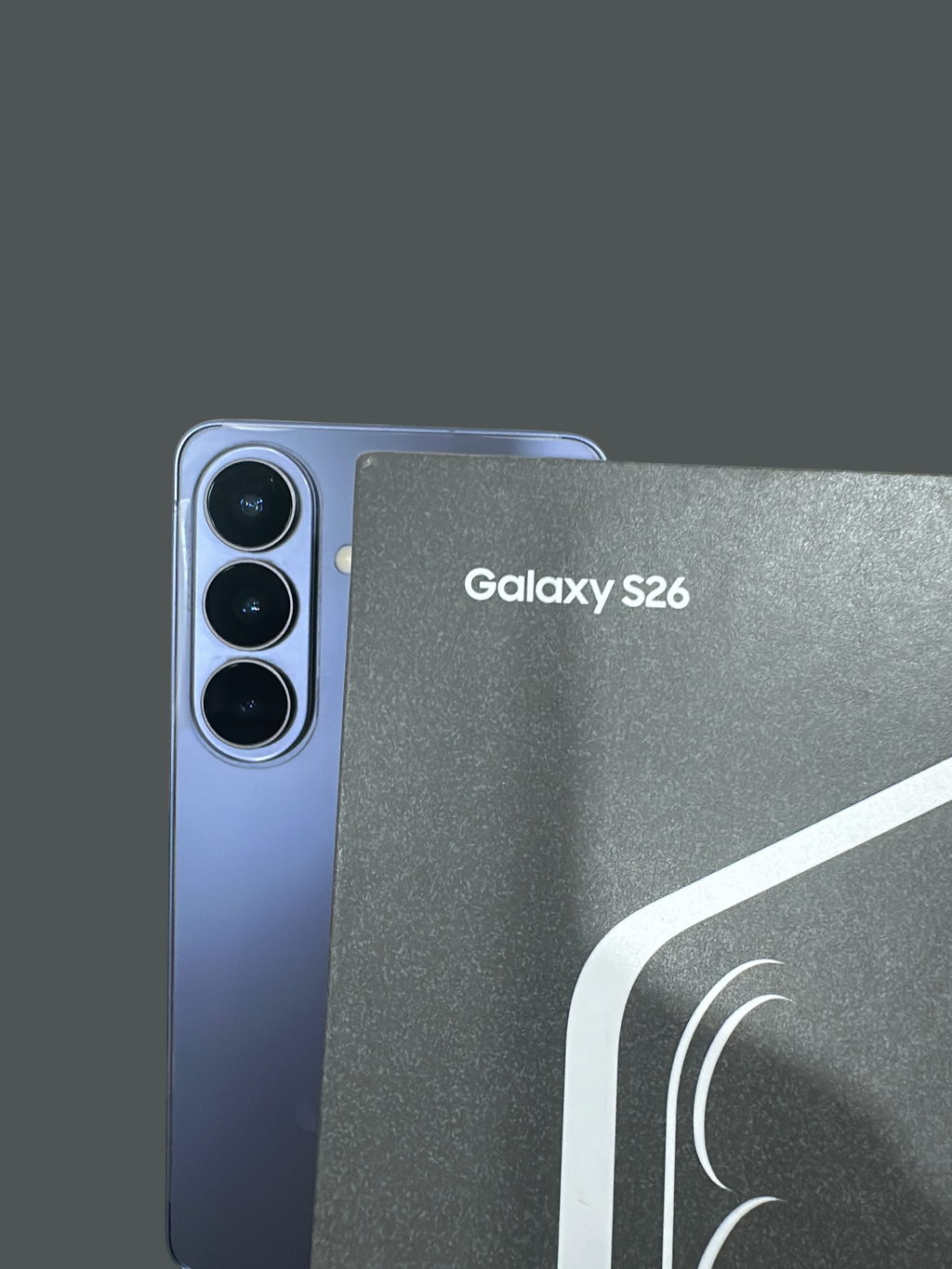 Iphoneio Official Samsung Galaxy S26 smartphone in light purple with a triple-lens camera system next to its box