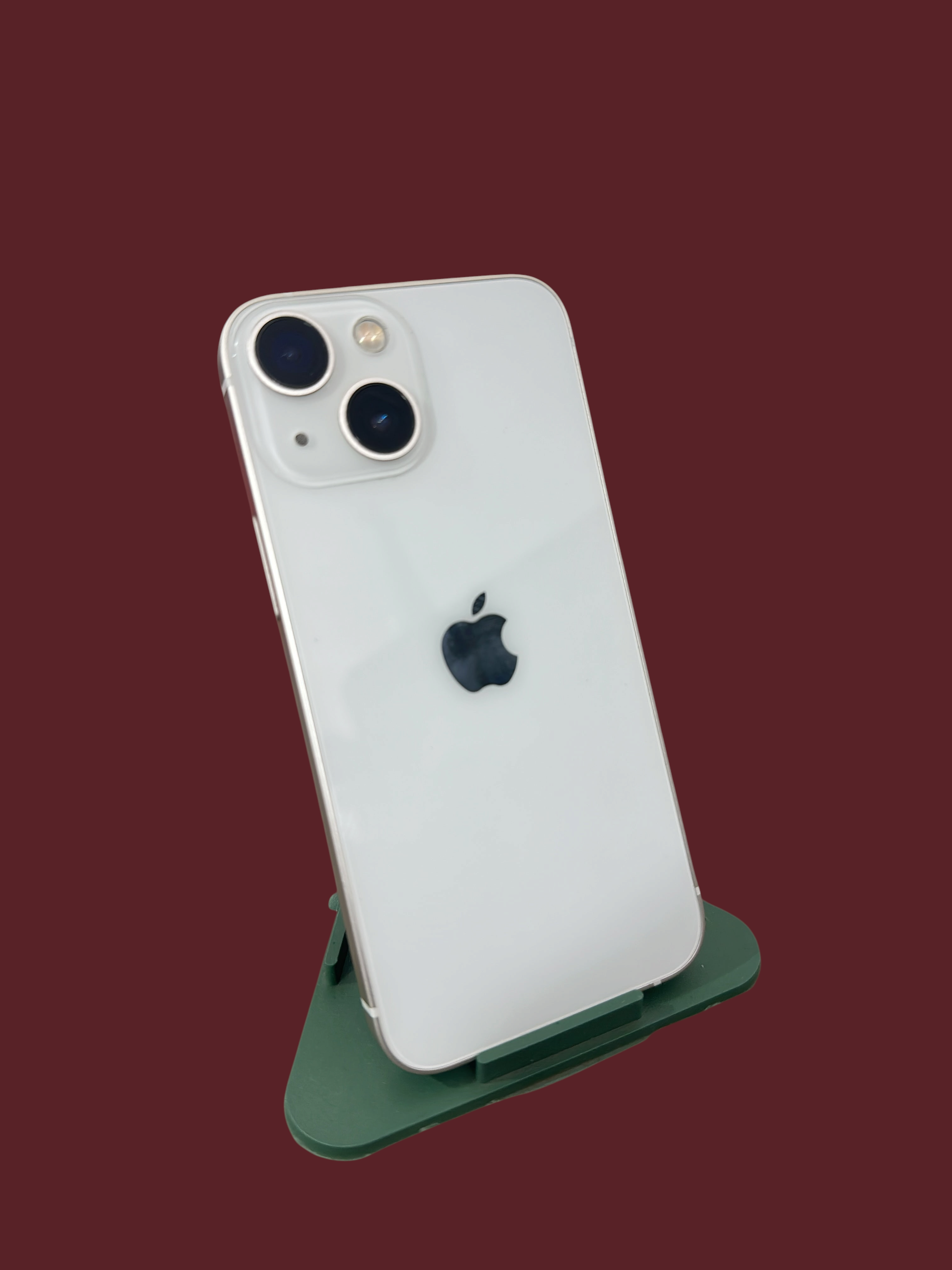 Iphoneio Official white smartphone with a dual-camera system and glass back, displayed on a green stand.